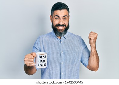 Young Hispanic Man Drinking Mug Of Coffee With Best Dad Ever Message Screaming Proud, Celebrating Victory And Success Very Excited With Raised Arm 