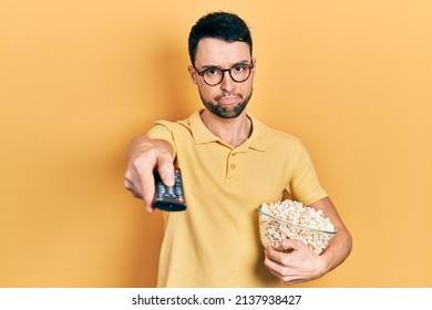 Young Hispanic Man Eating Popcorn Using Tv Control Depressed And Worry For Distress, Crying Angry And Afraid. Sad Expression. 