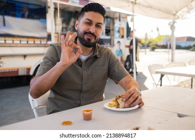 Young Hispanic Man Enjoying A Carnitas Taco Outside