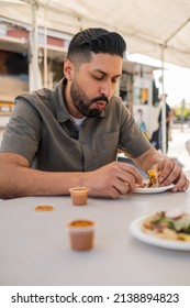 Young Hispanic Man Enjoying A Carnitas Taco Outside