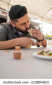 Young Hispanic Man Enjoying A Carnitas Taco Outside