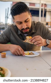 Young Hispanic Man Enjoying A Carnitas Taco Outside