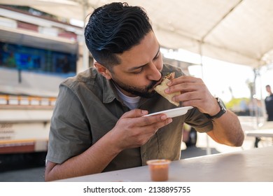 Young Hispanic Man Enjoying A Carnitas Taco Outside