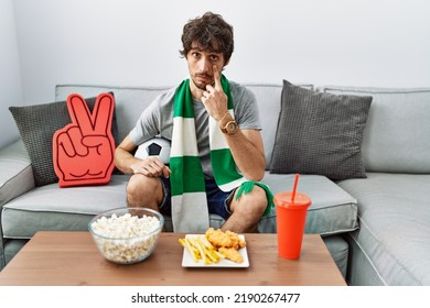 Young Hispanic Man Football Hooligan Cheering Game At Home Pointing To The Eye Watching You Gesture, Suspicious Expression 