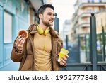 Young hispanic man having breakfast using headphones at the city.