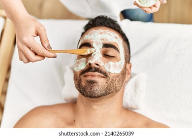 Young hispanic man having facial mask treatment at beauty center - Powered by Shutterstock