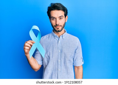 Young Hispanic Man Holding Blue Ribbon Thinking Attitude And Sober Expression Looking Self Confident 