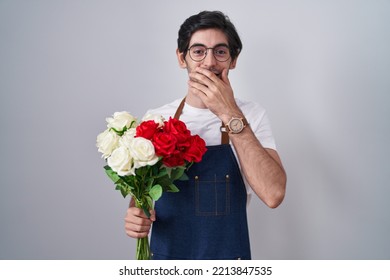 Young Hispanic Man Holding Bouquet Of White And Red Roses Laughing And Embarrassed Giggle Covering Mouth With Hands, Gossip And Scandal Concept 