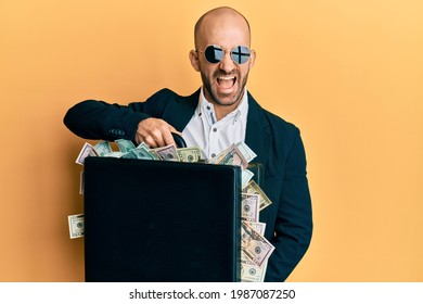 Young hispanic man holding briefcase with dollars smiling and laughing hard out loud because funny crazy joke. 