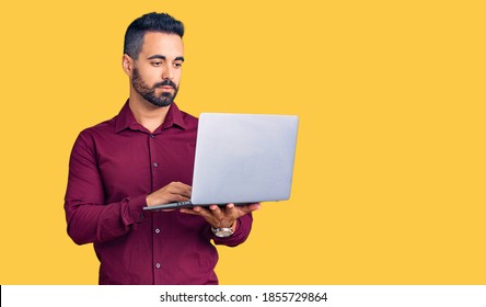 Young Hispanic Man Holding Laptop Thinking Attitude And Sober Expression Looking Self Confident 