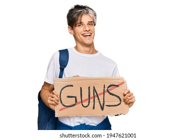 Young Hispanic Man Holding No Guns Warning Banner Looking Positive And Happy Standing And Smiling With A Confident Smile Showing Teeth 