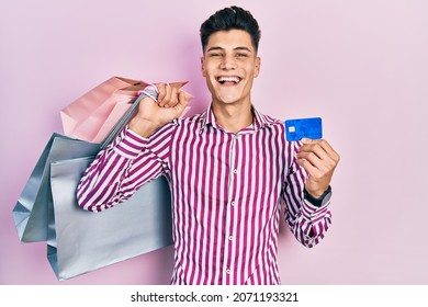 Young Hispanic Man Holding Shopping Bags And Credit Card Celebrating Crazy And Amazed For Success With Open Eyes Screaming Excited. 