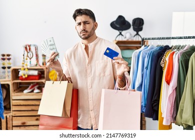 Young Hispanic Man Holding Shopping Bags And Credit Card Clueless And Confused Expression. Doubt Concept. 