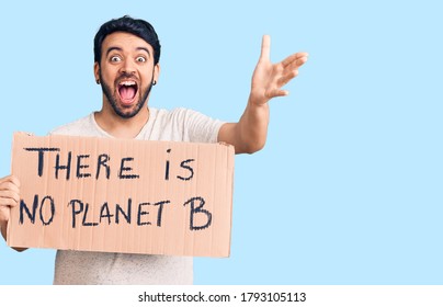 Young Hispanic Man Holding There Is No Planet B Banner Celebrating Victory With Happy Smile And Winner Expression With Raised Hands 