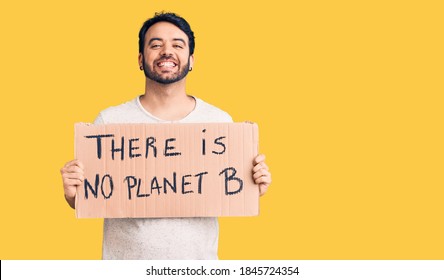 Young Hispanic Man Holding There Is No Planet B Banner Looking Positive And Happy Standing And Smiling With A Confident Smile Showing Teeth 