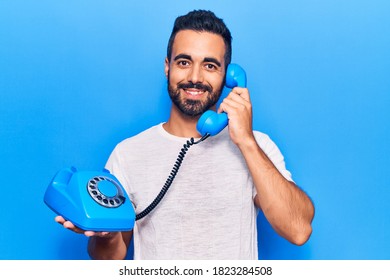 Young hispanic man holding vintage telephone looking positive and happy standing and smiling with a confident smile showing teeth  - Powered by Shutterstock