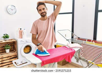 Young Hispanic Man Ironing Clothes At Home Confuse And Wondering About Question. Uncertain With Doubt, Thinking With Hand On Head. Pensive Concept. 