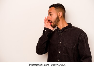 Young hispanic man isolated on white background is saying a secret hot braking news and looking aside
