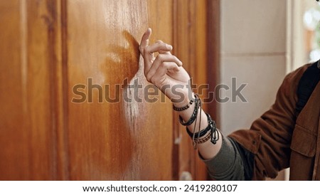 Young hispanic man knocking on the door at street