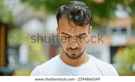 Young hispanic man looking down with serious expression at park