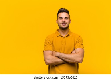 young hispanic man looking like a happy, proud and satisfied achiever smiling with arms crossed against orange wall - Powered by Shutterstock