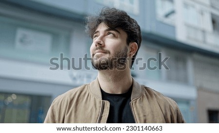 Young hispanic man looking to the sky with serious expression and winner expression at street