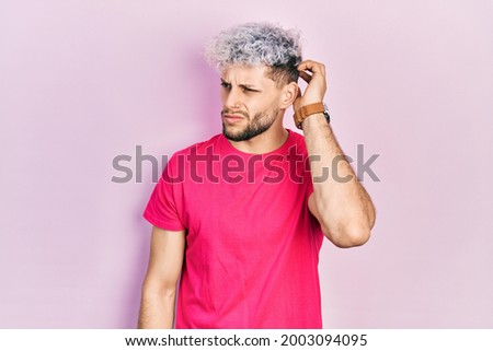 Young hispanic man with modern dyed hair wearing casual pink t shirt confuse and wondering about question. uncertain with doubt, thinking with hand on head. pensive concept. 