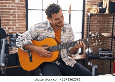 Músico joven hispano tocando guitarra clásica en estudio de música