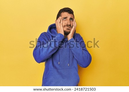 Young Hispanic man on yellow background whining and crying disconsolately.