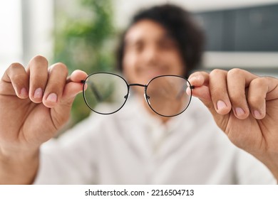 Young Hispanic Man Optician Holding Glasses At Clinic