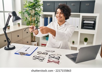 Young Hispanic Man Optician Holding Glasses At Clinic