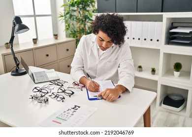 Young Hispanic Man Optician Writing On Clipboard At Clinic