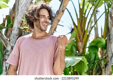 Young Hispanic Man Outdoors On A Sunny Day Pointing Thumb Up To The Side Smiling Happy With Open Mouth 