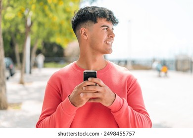 Young hispanic man at outdoors using mobile phone and looking up - Powered by Shutterstock