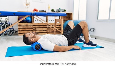 Young Hispanic Man Patient Having Neck Rehab Session Using Foam Roller At Clinic