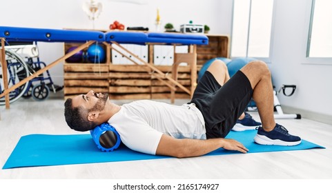 Young Hispanic Man Patient Smiling Confident Having Neck Rehab Session Using Foam Roller At Clinic