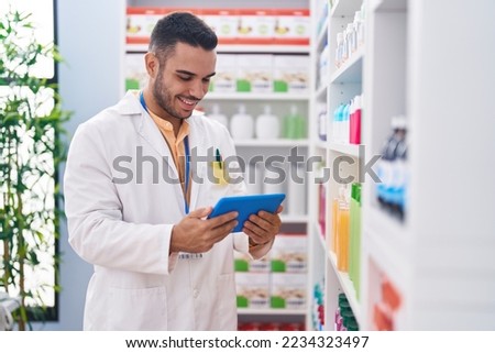 Young hispanic man pharmacist using touchpad working at pharmacy