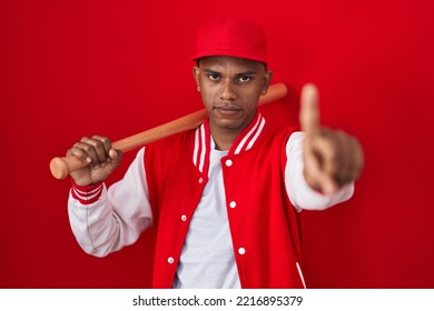 Young hispanic man playing baseball holding bat pointing with finger up and angry expression, showing no gesture  - Powered by Shutterstock