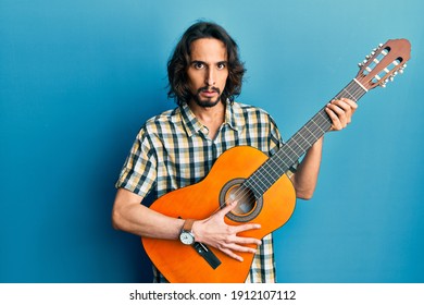 Young hispanic man playing classical guitar clueless and confused expression. doubt concept. 