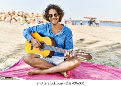 Young hispanic man playing classical guitar sitting on sand at the beach. - Powered by Shutterstock