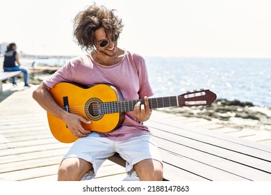 Young hispanic man playing classical guitar sitting on  bench at the beach.