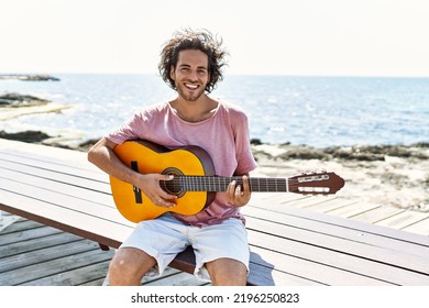 Young hispanic man playing classical guitar sitting on  bench at the beach. - Shutterstock ID 2196250823