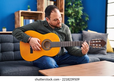 Young Hispanic Man Playing Classical Guitar Sitting On Bed At Home