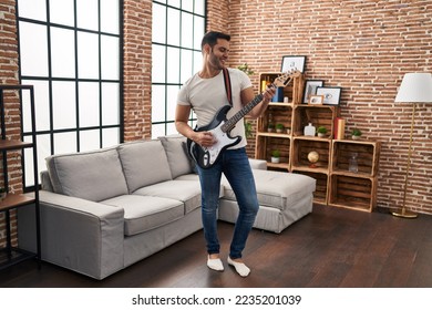 Young hispanic man playing electrical guitar standing at home