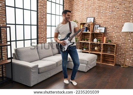 Young hispanic man playing electrical guitar standing at home