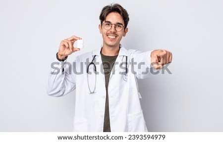 young hispanic man pointing at camera choosing you. physician with pills bottle concept