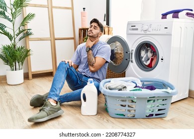 Young Hispanic Man Putting Dirty Laundry Into Washing Machine Touching Painful Neck, Sore Throat For Flu, Clod And Infection 