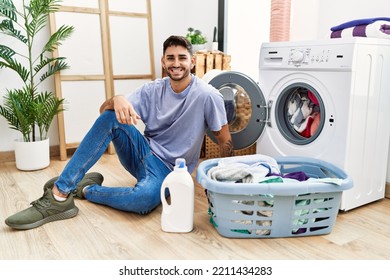 Young Hispanic Man Putting Dirty Laundry Into Washing Machine With A Happy And Cool Smile On Face. Lucky Person. 