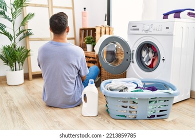 Young Hispanic Man Putting Dirty Laundry Into Washing Machine Standing Backwards Looking Away With Crossed Arms 