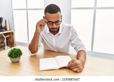 Young Hispanic Man Reading Book At Office